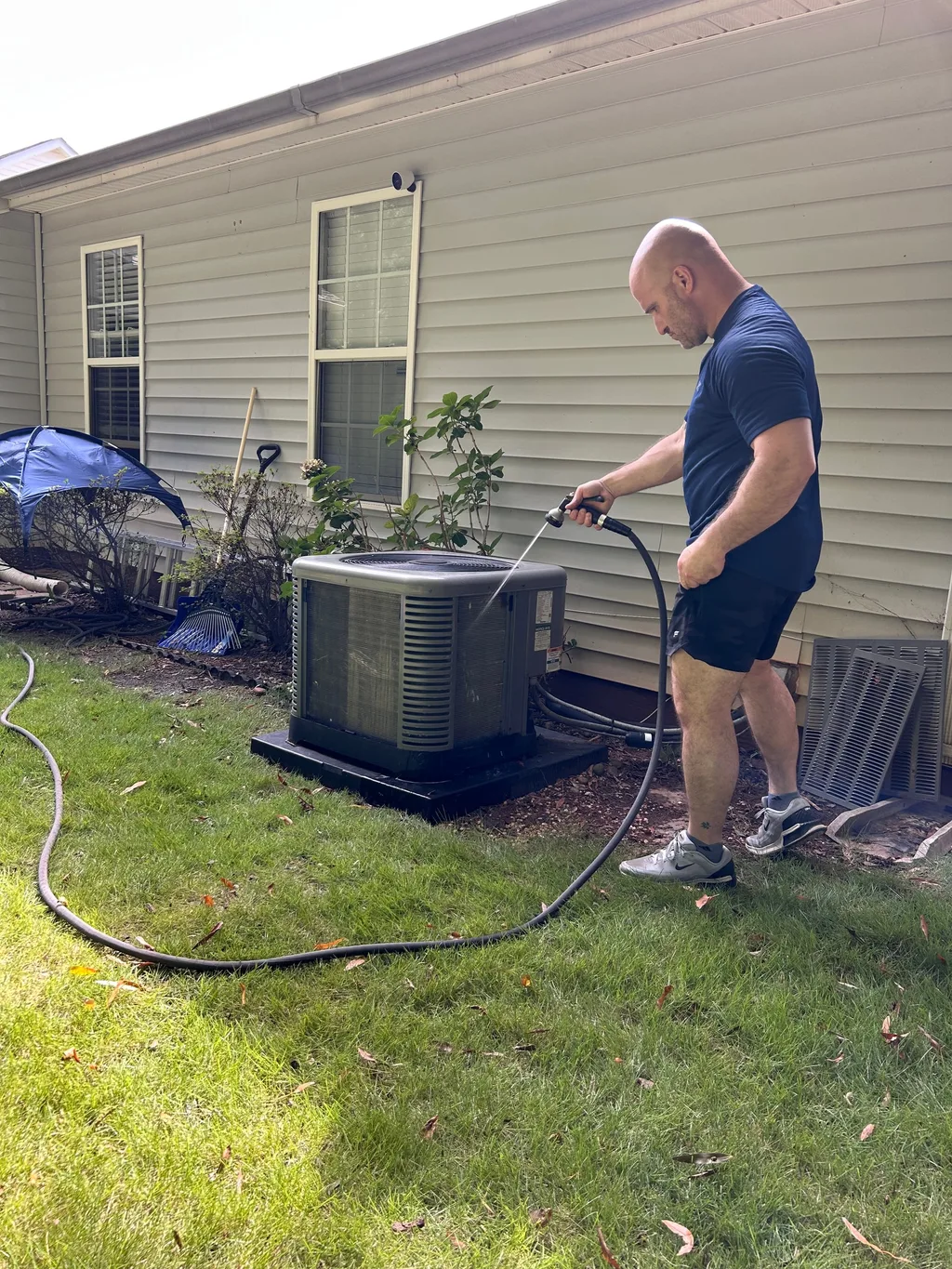 Technician rinsing the coil of an outdoor condenser unit with a garden hose