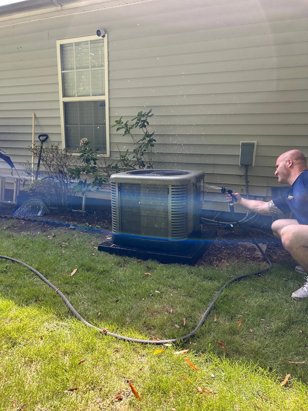 Water spraying across the fins of an outdoor condenser unit during a coil rinse