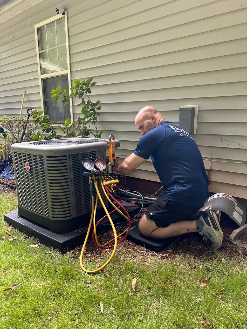 Technician kneeling at an opened outdoor condenser with manifold gauges attached to the service ports