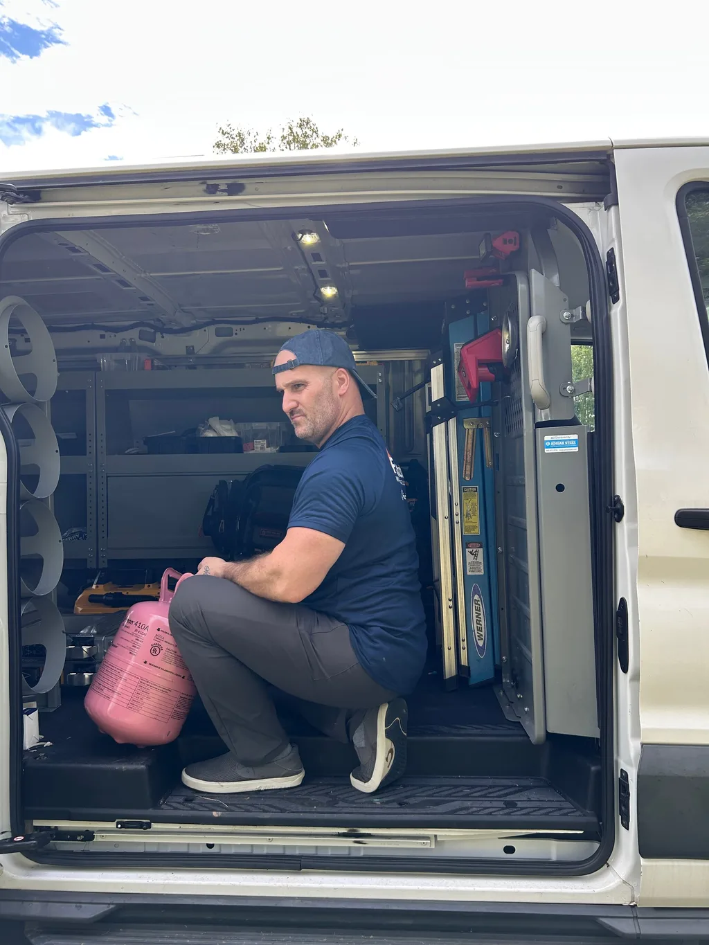 Jason crouched in the back of the work van holding a refrigerant cylinder